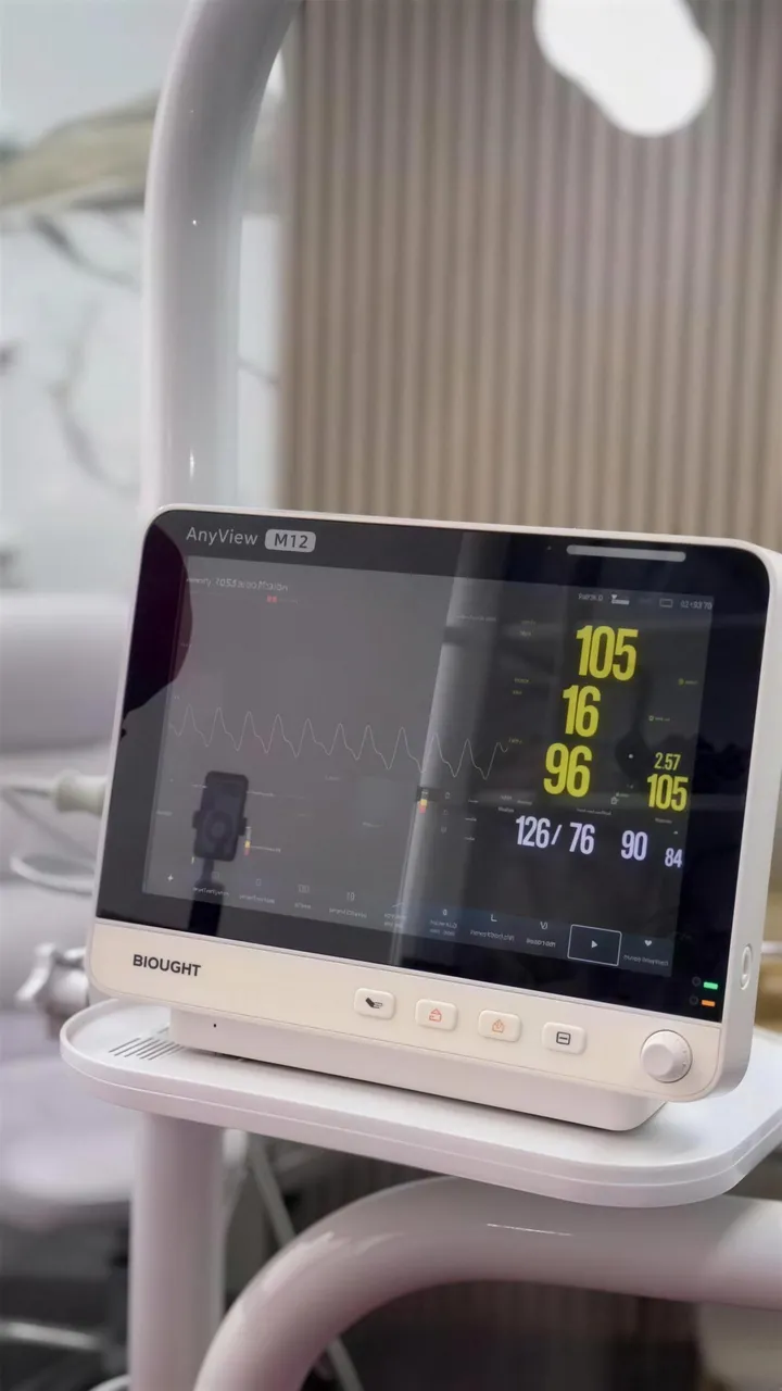 Monitor de sinais vitais ao lado da maca no consultório da Dra. Letícia