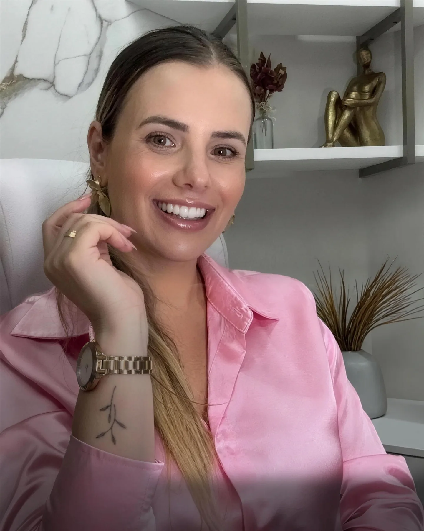 Dra. Letícia Hellen sorrindo no consultório, com estante de esculturas douradas ao fundo